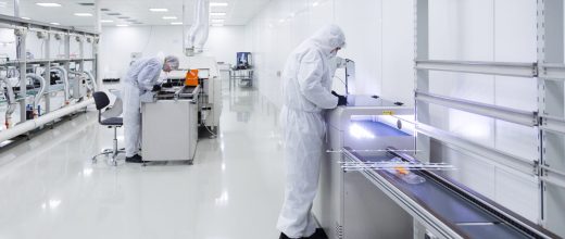 factory workers in white lab suits and black latex gloves, working with some modern equipment in a very clean room.